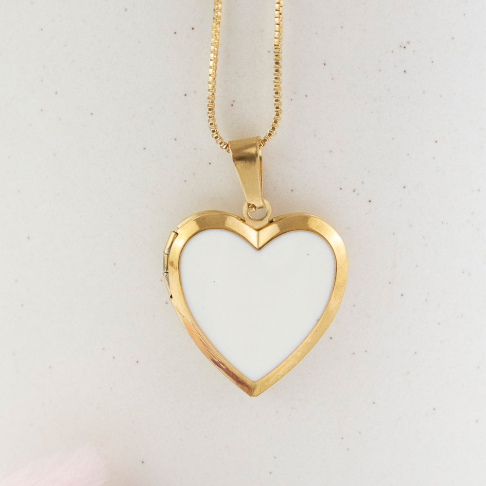 Collar relicario en forma de corazón con interior blanco, para colocar fotos dentro de el. Collar en tono dorado/acero